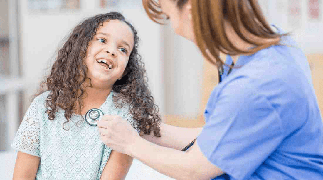 A pediatric resident checking in on her patient with a stethoscope.